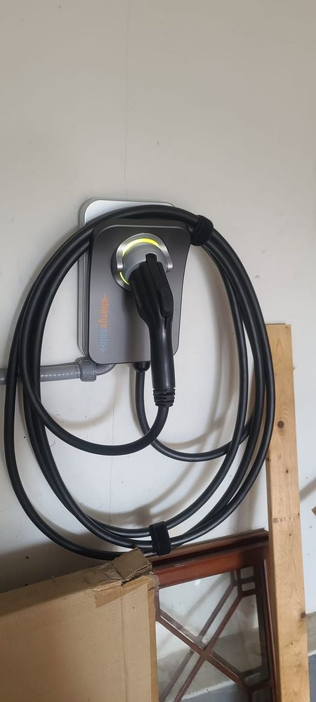 Hand using a yellow drill to install a brass door latch on a gray door frame