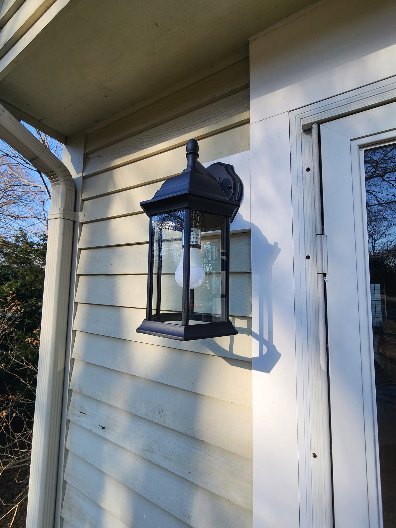 Black outdoor lantern on white house siding beside a door under the eave