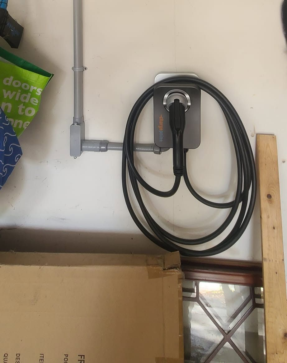 Coiled black cable on a wall-mounted hook beside metal conduit and a wooden plank indoors