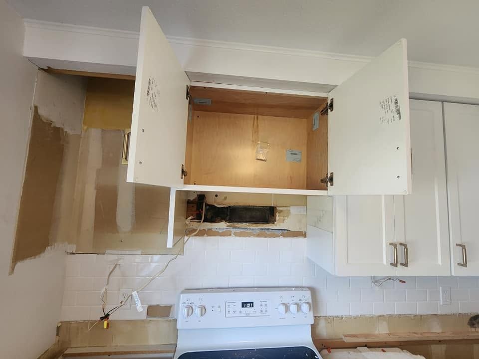 Open kitchen cabinets above a stove with a damaged wall and exposed opening between them