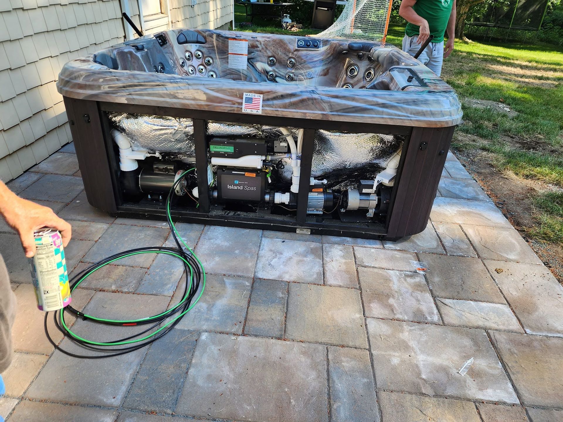 Burned hot tub on a patio, with a person holding a can at the left edge and hoses in front