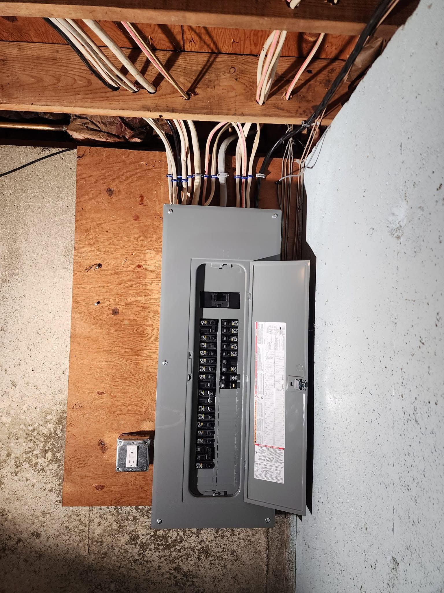 Open electrical breaker panel with exposed wiring in a basement wall.
