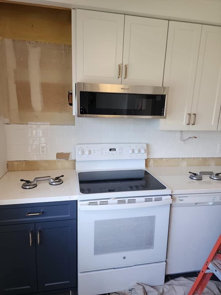 Kitchen with white stove and cabinets, dark lower cabinets, and a microwave above the range.