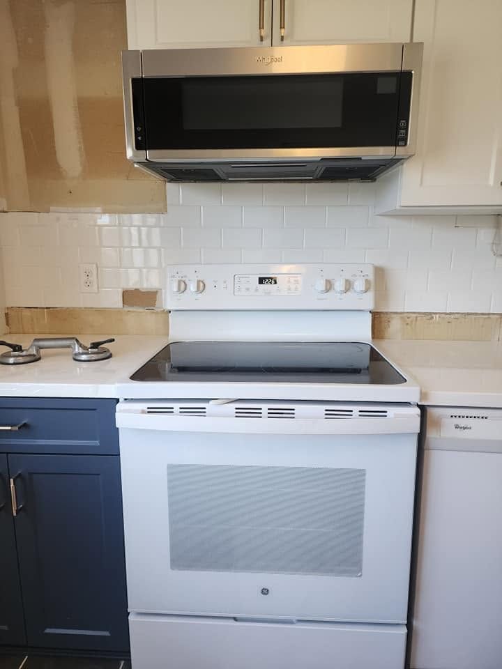 White kitchen with black stove, microwave, and dark lower cabinets against white tile backsplash.