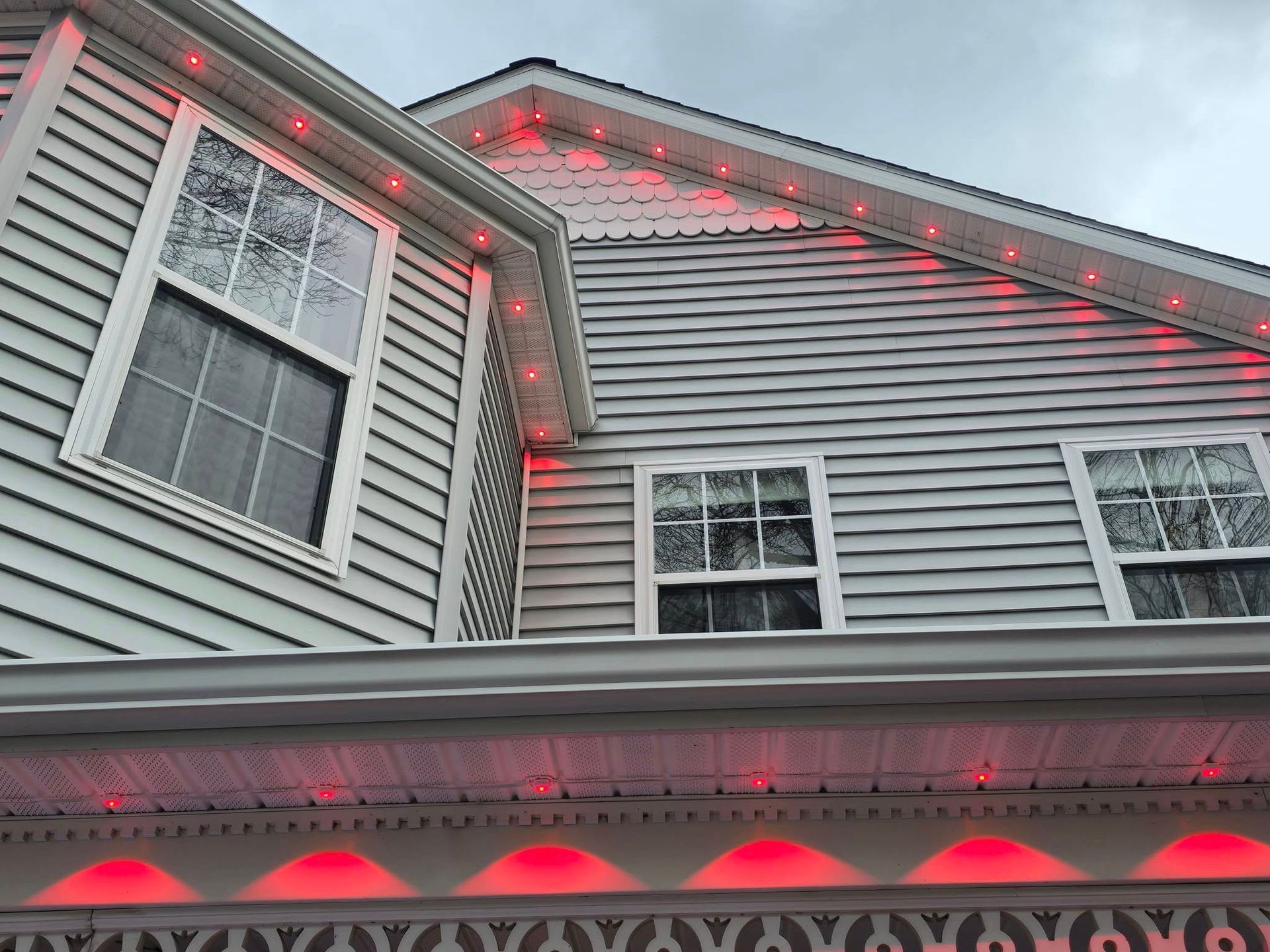 Gray house exterior with red holiday lights along the roofline and windows at dusk