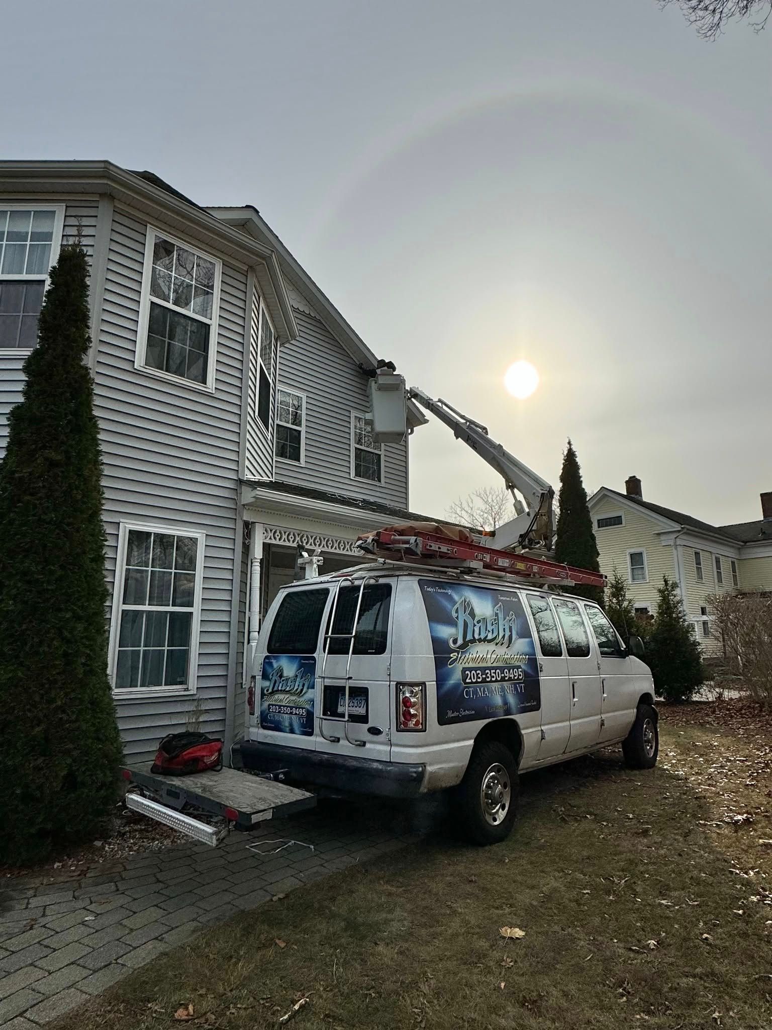 Work van with ladder parked beside a house at sunset under a faint rainbow