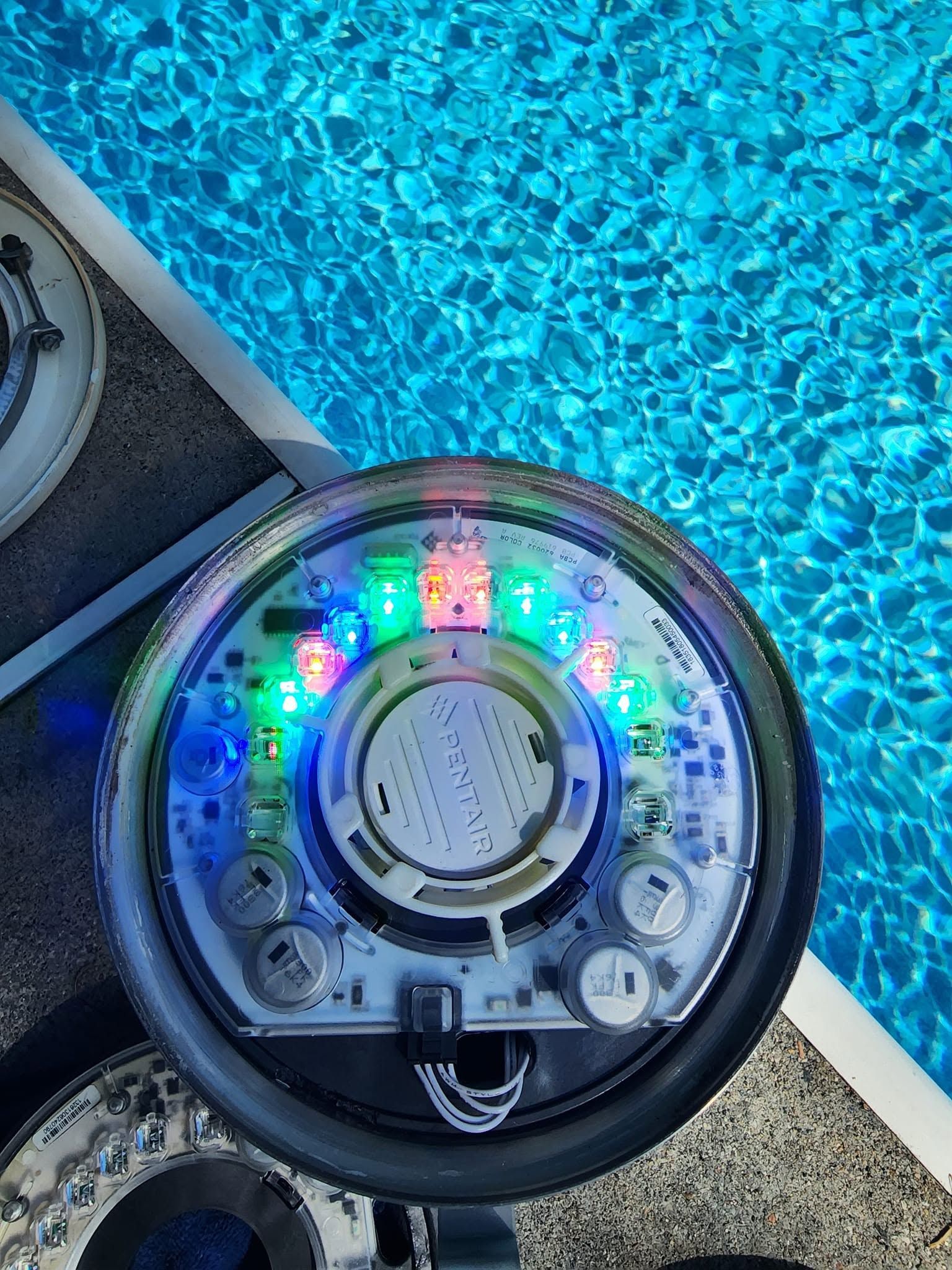 Colorful LED-lit pool float or robot toy floating beside a bright blue swimming pool