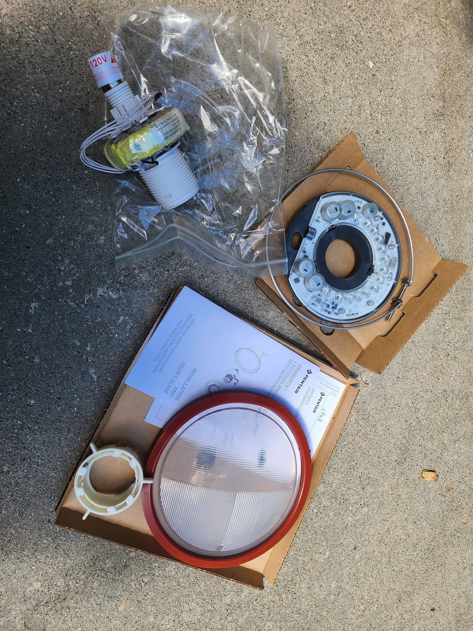 Assorted ring-shaped parts and packaging on concrete, including a red-rimmed cover and coiled components