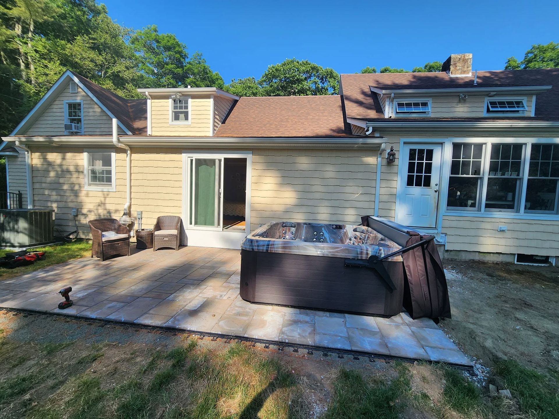Back patio with outdoor chairs, a hot tub, and a house’s sliding glass doors in sunlight