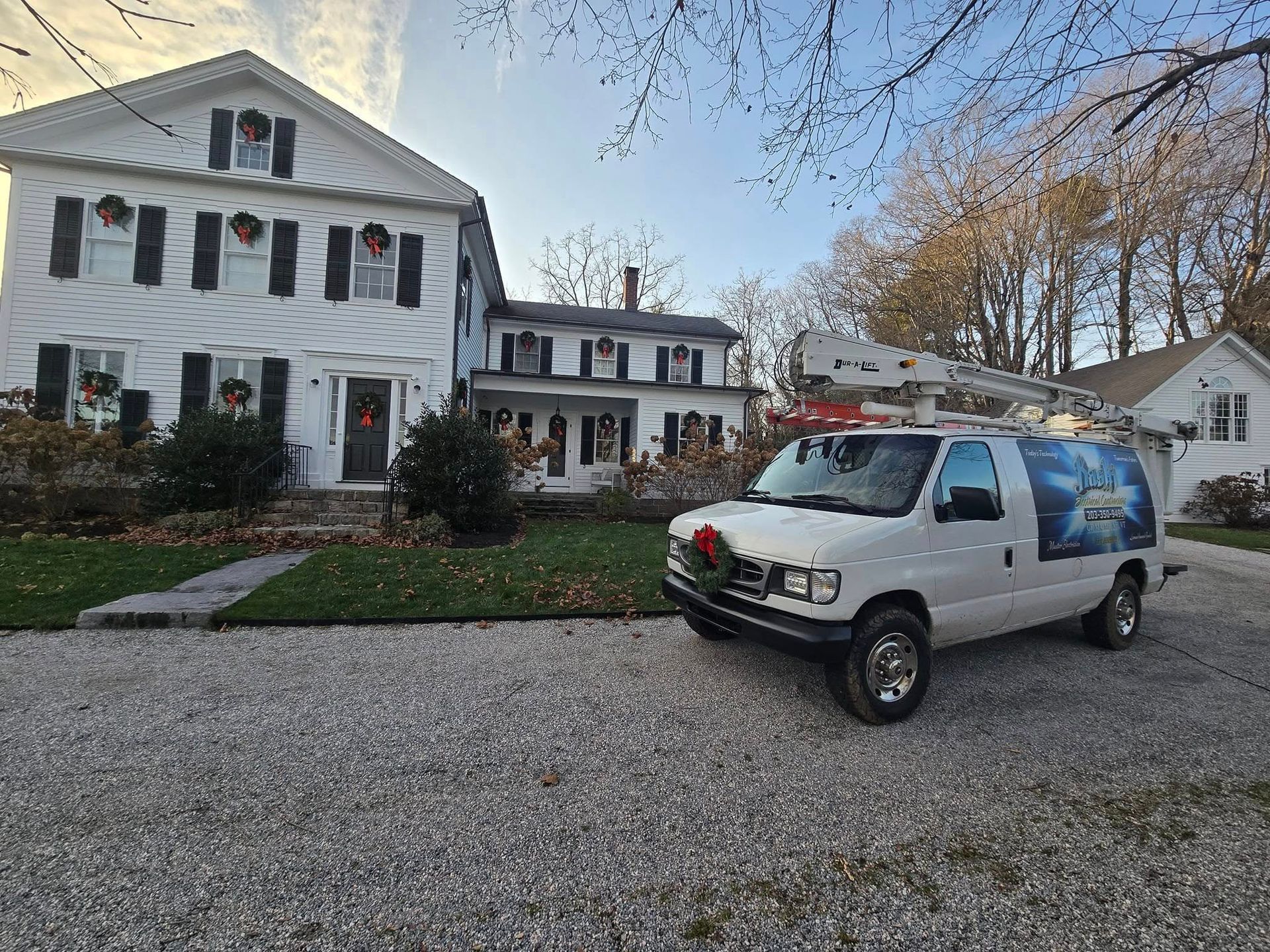 White house with black shutters and a silver service van parked on a gravel driveway at dusk