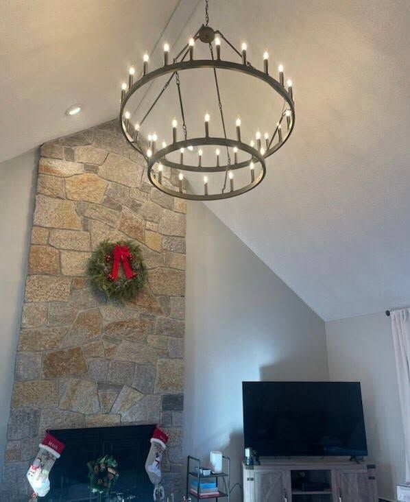 Living room with stone fireplace, Christmas wreath, TV, and a black chandelier on a vaulted ceiling