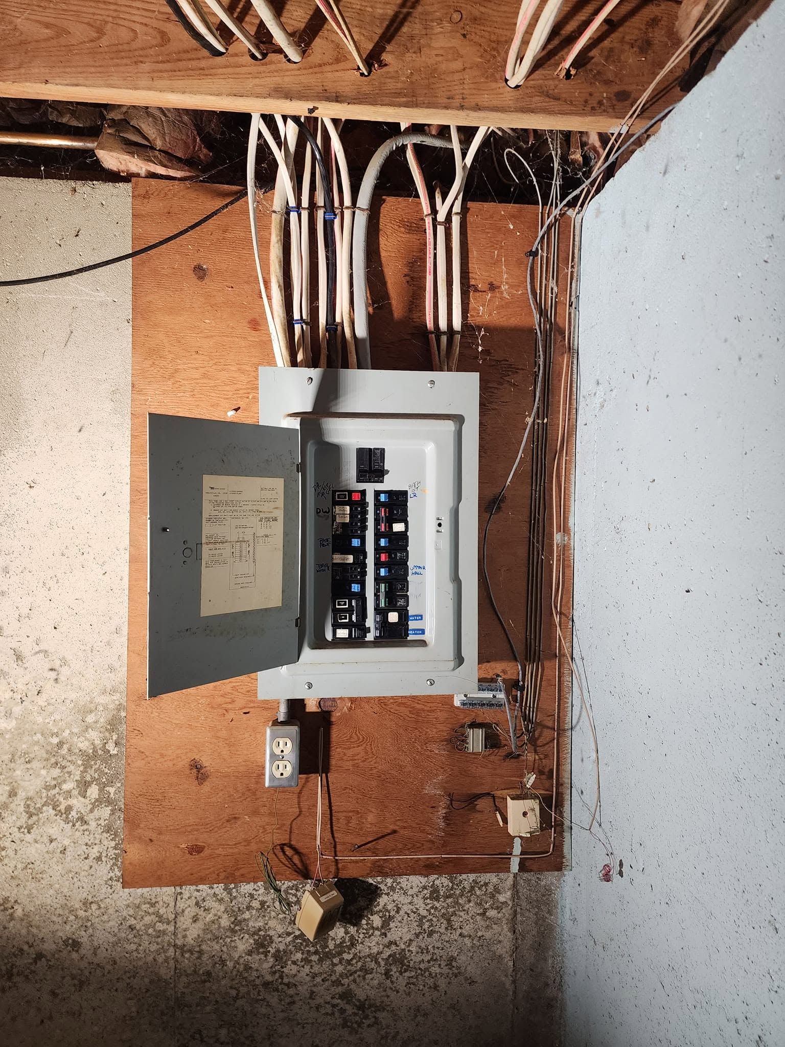 Open electrical breaker panel in unfinished wall with exposed wiring above and below