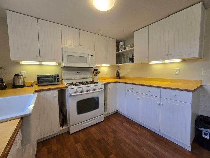 Small L-shaped kitchen with white cabinets, wood countertops, gas stove, and hardwood floor