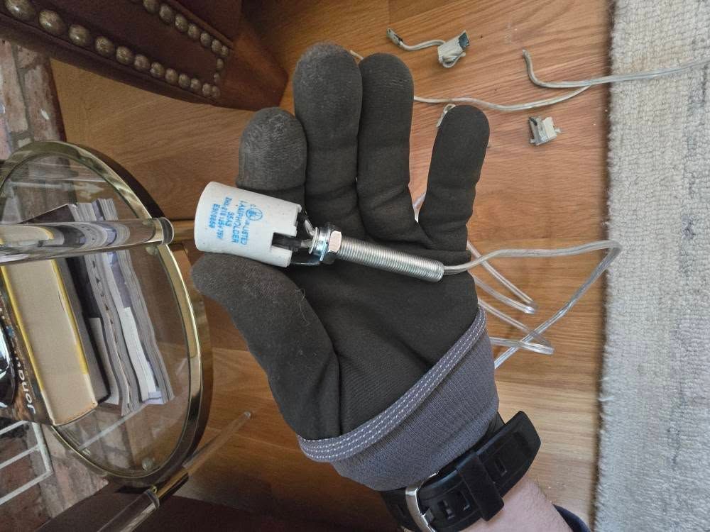 Gloved hand holding a small white sensor on a wooden table with cables and medical items nearby