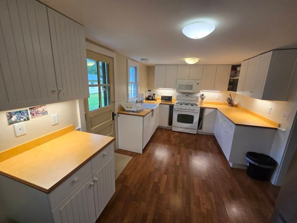 Bright kitchen with wood floors, white cabinets, wooden countertops, and a stove at the far end.