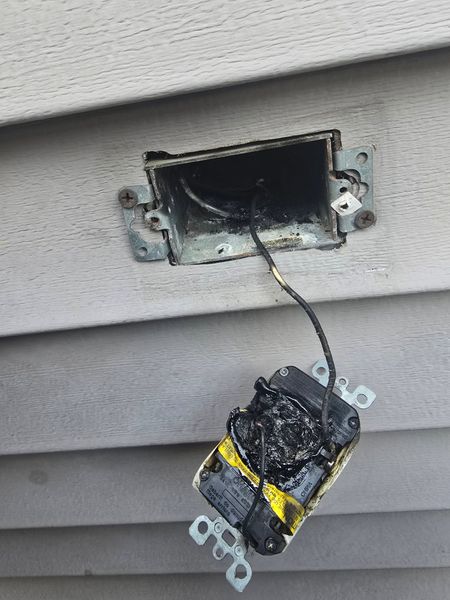 Hand using a yellow drill to install a brass door latch on a gray door frame