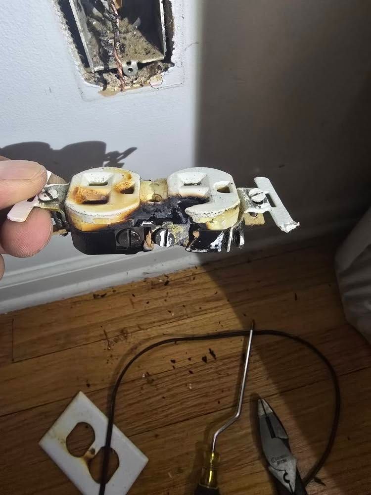 Damaged wall outlet with exposed wiring and tools on the floor nearby.