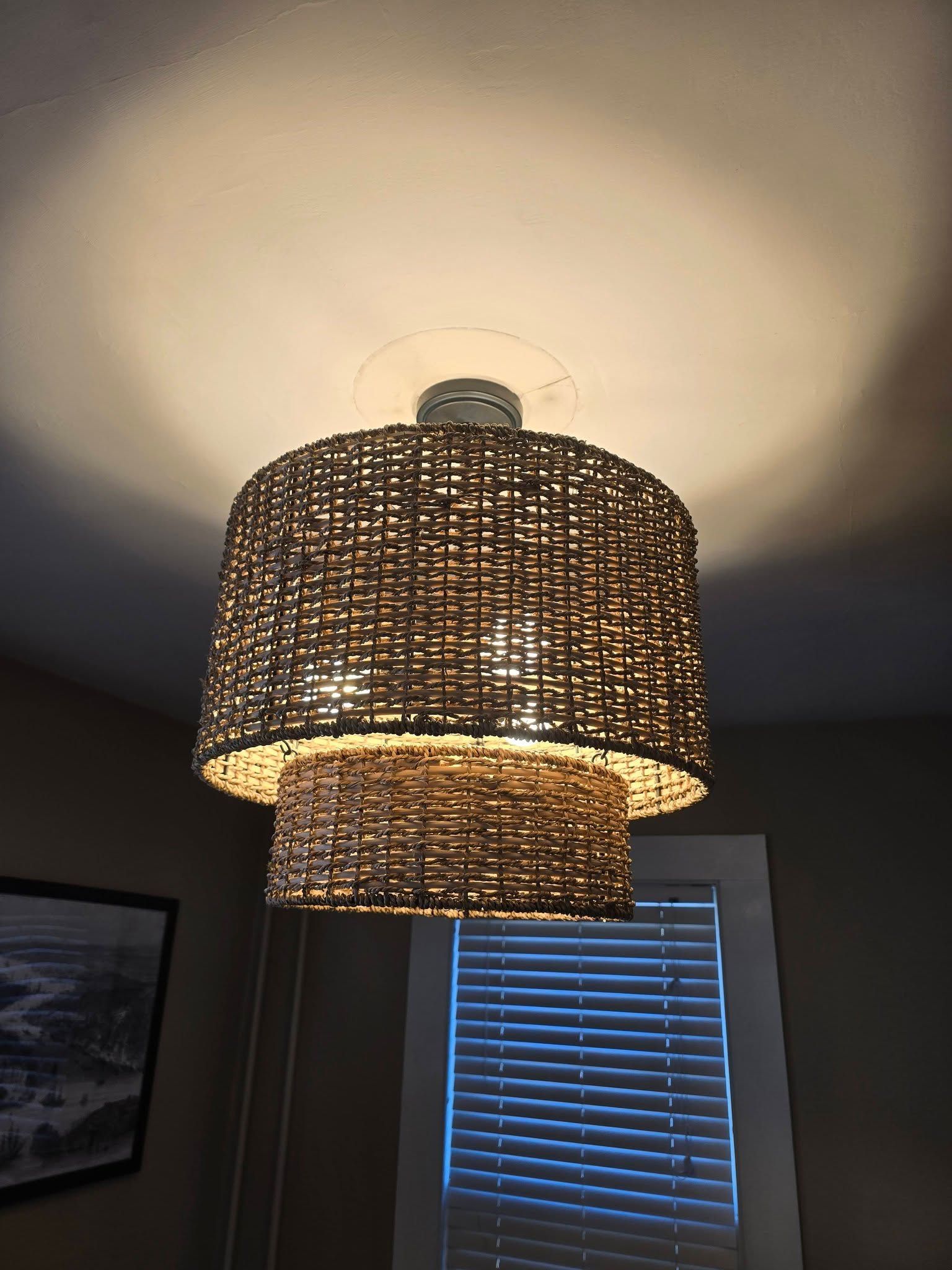 Woven wicker pendant lamp casting warm light over a window with blinds