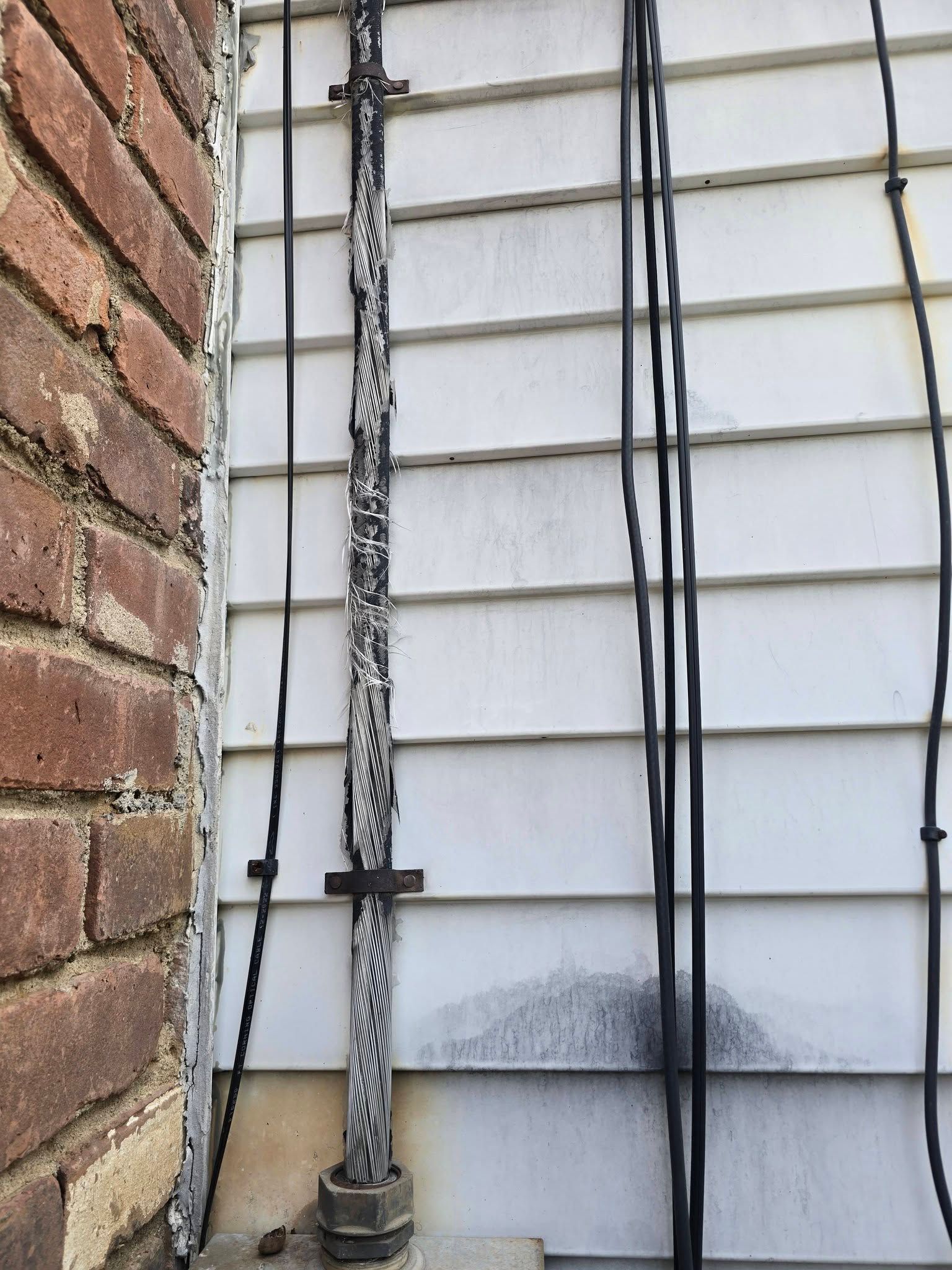 Brick wall and white siding with electrical conduit and cables running vertically along the wall.