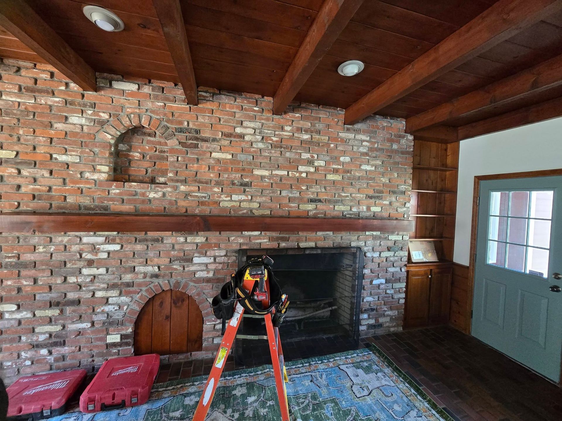 Brick fireplace in a rustic room, with a ladder and tools in front of it.