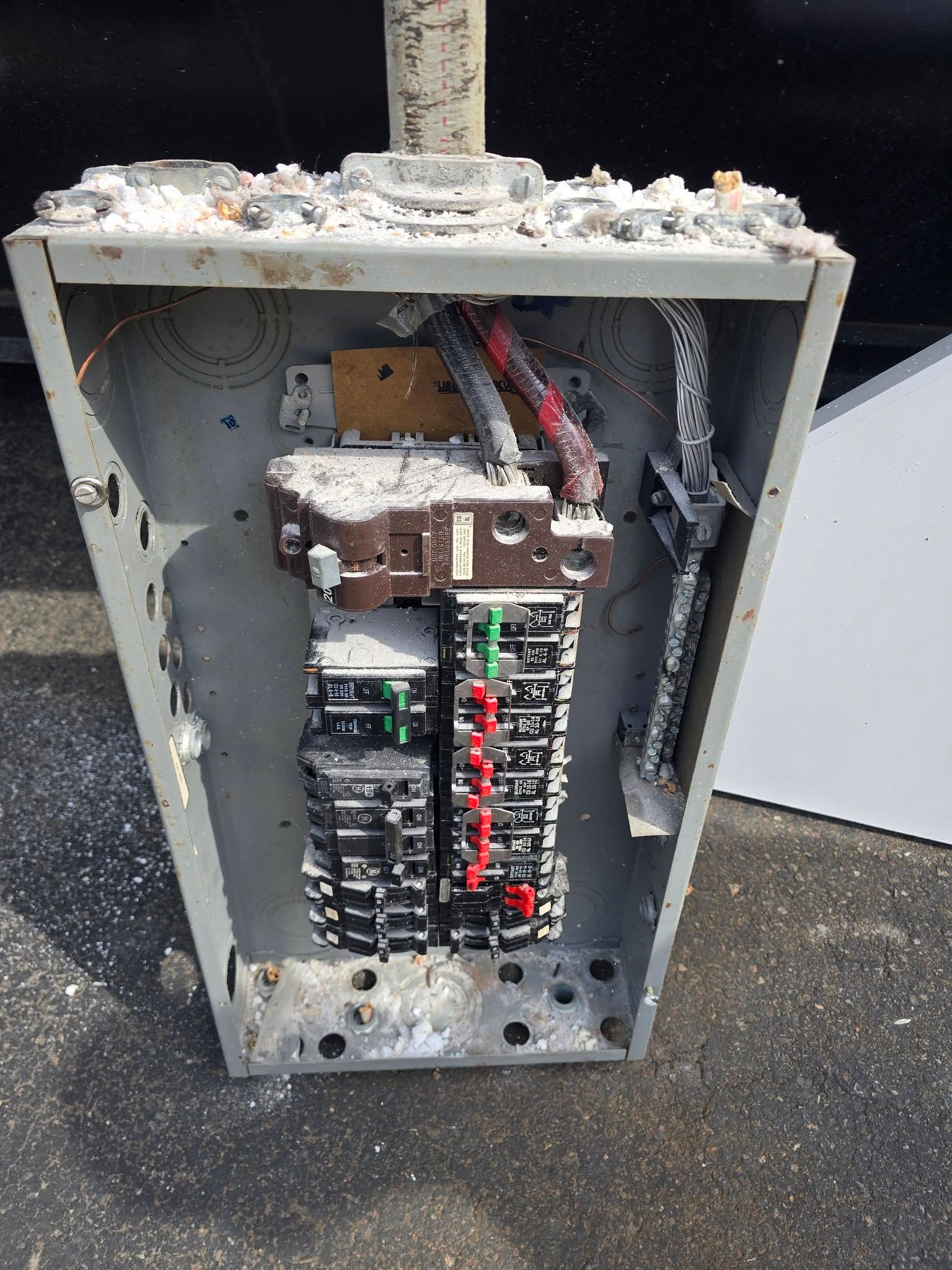 Open electrical panel with exposed wiring and circuit breakers in a gray metal cabinet