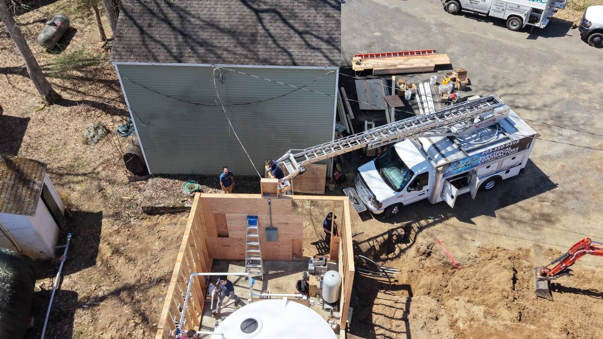 Aerial view of a construction site with a crane truck beside a large wall panel and wooden foundation forms.