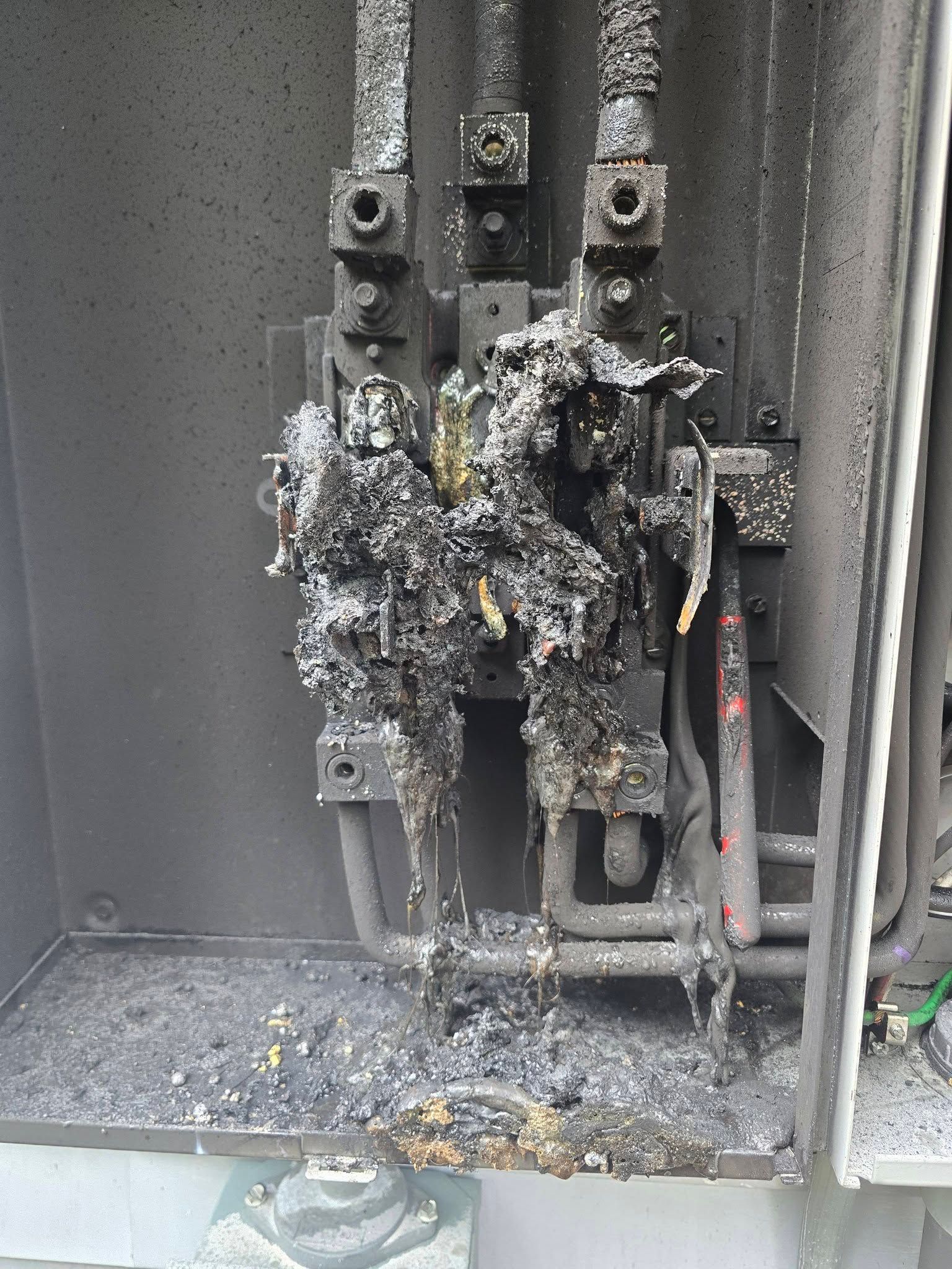 Charred electrical panel with melted wiring and soot damage inside a metal cabinet