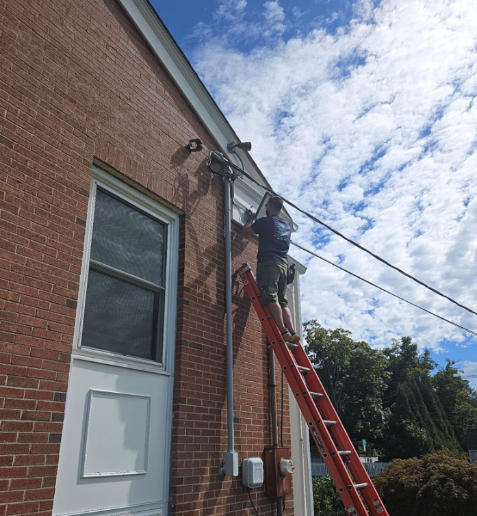 Worker on a red ladder repairing cables on a brick building under a cloudy sky