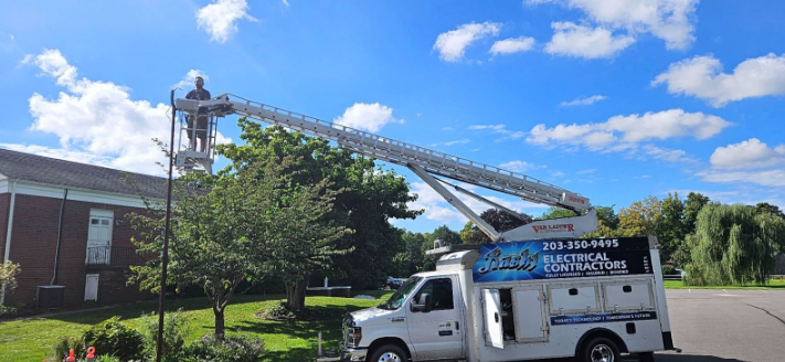 Utility truck with extended ladder parked beside a brick building under a blue sky