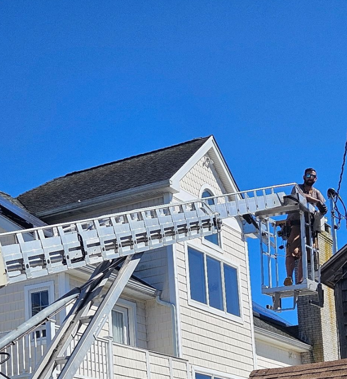 Worker in a bucket lift repairing a white house roof under a clear blue sky