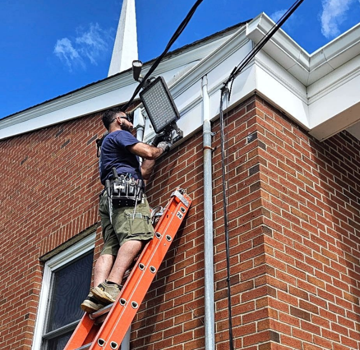 Worker on a ladder installing a light on the brick exterior of a building.