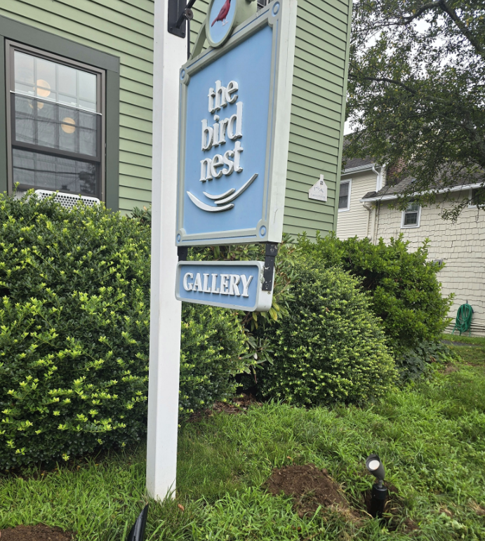 The Bird Nest Gallery sign beside a green house and shrubs
