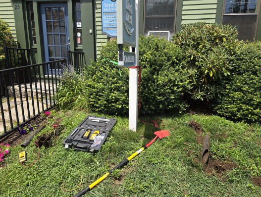 Utility box and red arrow marker in a grassy yard beside a house and railing.