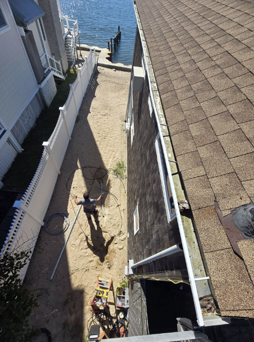Narrow sandy alley between buildings leading to the water, with a person and tools casting long shadows.