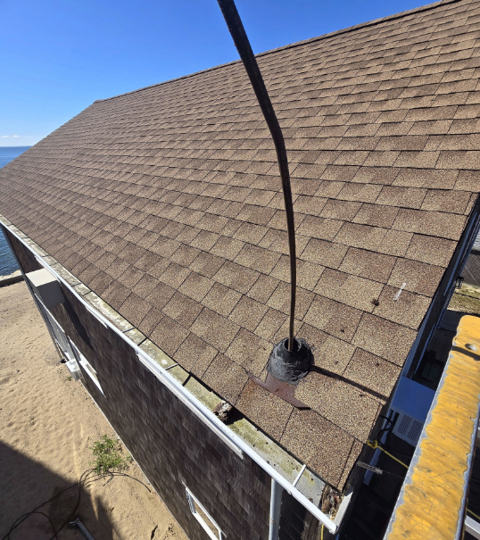 Roof shingles with a black vent pipe on a sloped house roof near the beach