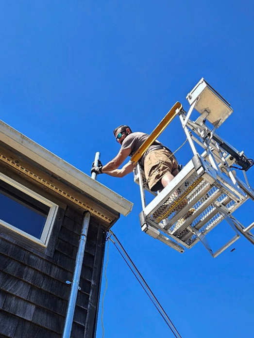 Worker on a lift painting the exterior of a house against a bright blue sky