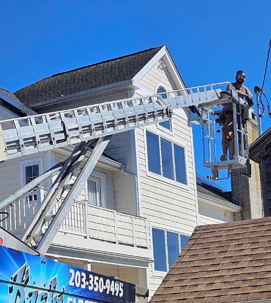 Worker on a lift repairing the exterior of a white house under a blue sky