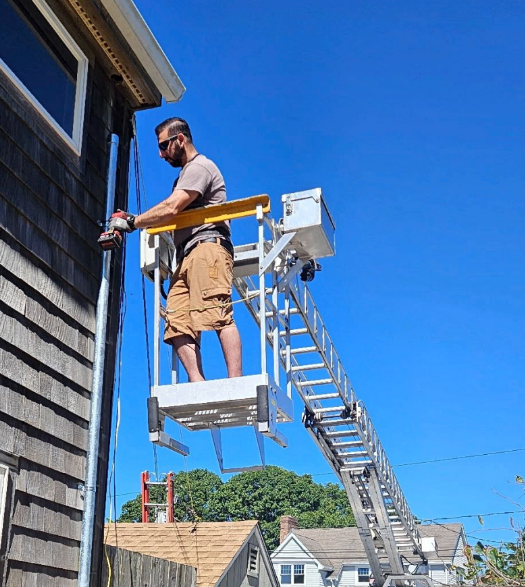 Man on a lift painting the side of a house under a clear blue sky