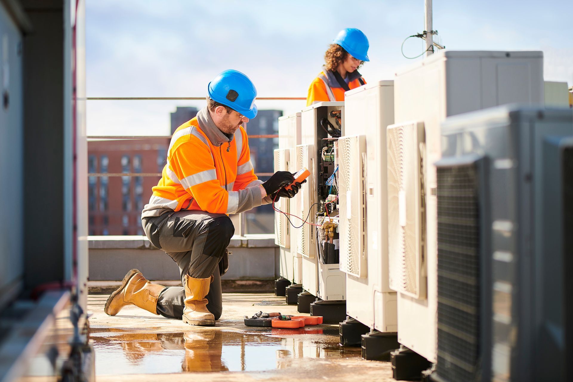 Two HVAC technicians in safety gear work on rooftop equipment.