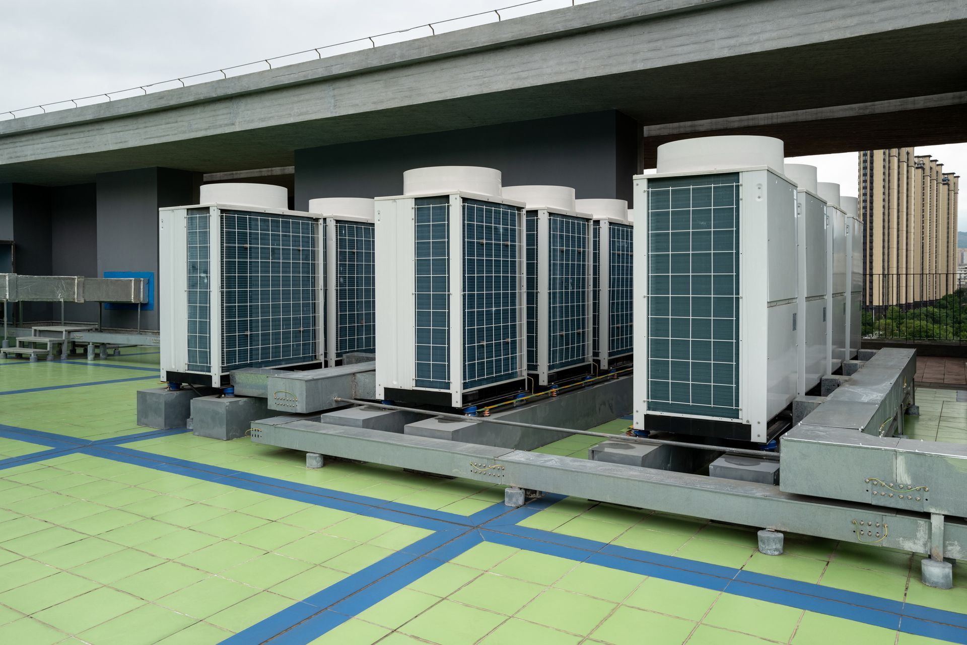 Air conditioning units on a rooftop, white and grey, green and blue flooring.