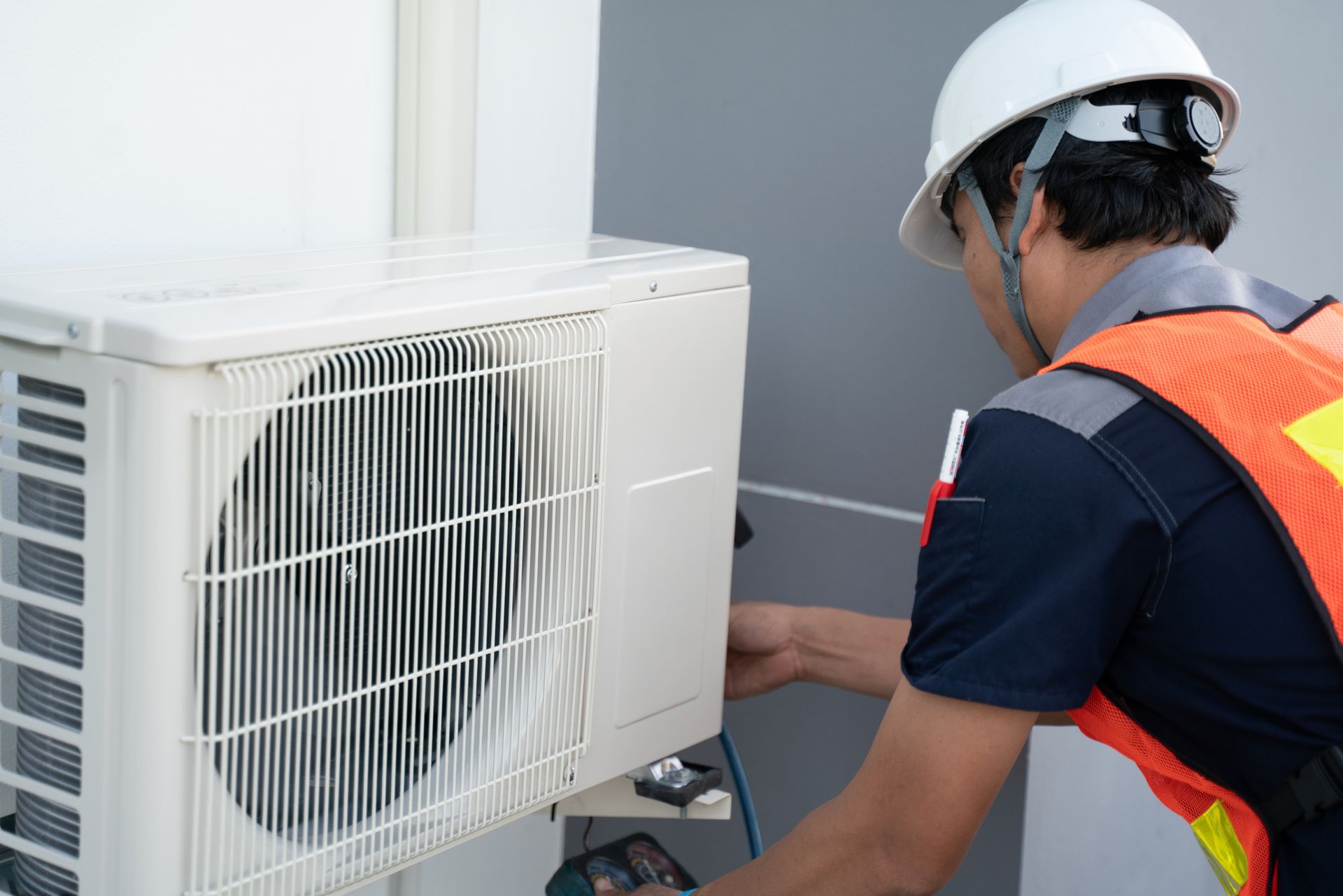 HVAC technician in hard hat and safety vest working on an outdoor air conditioning unit.