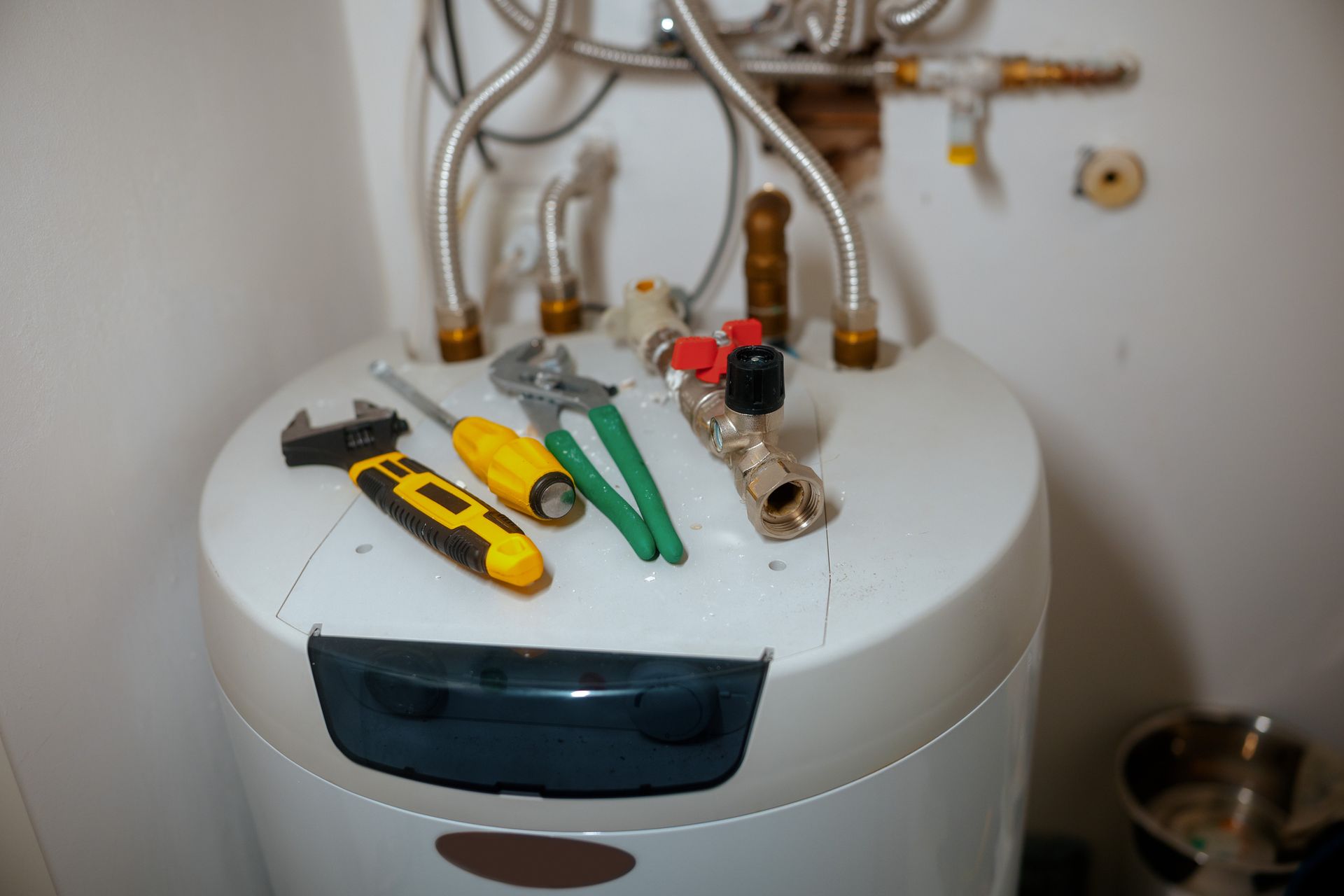 Tools on top of a white water heater, plumbing work in progress.