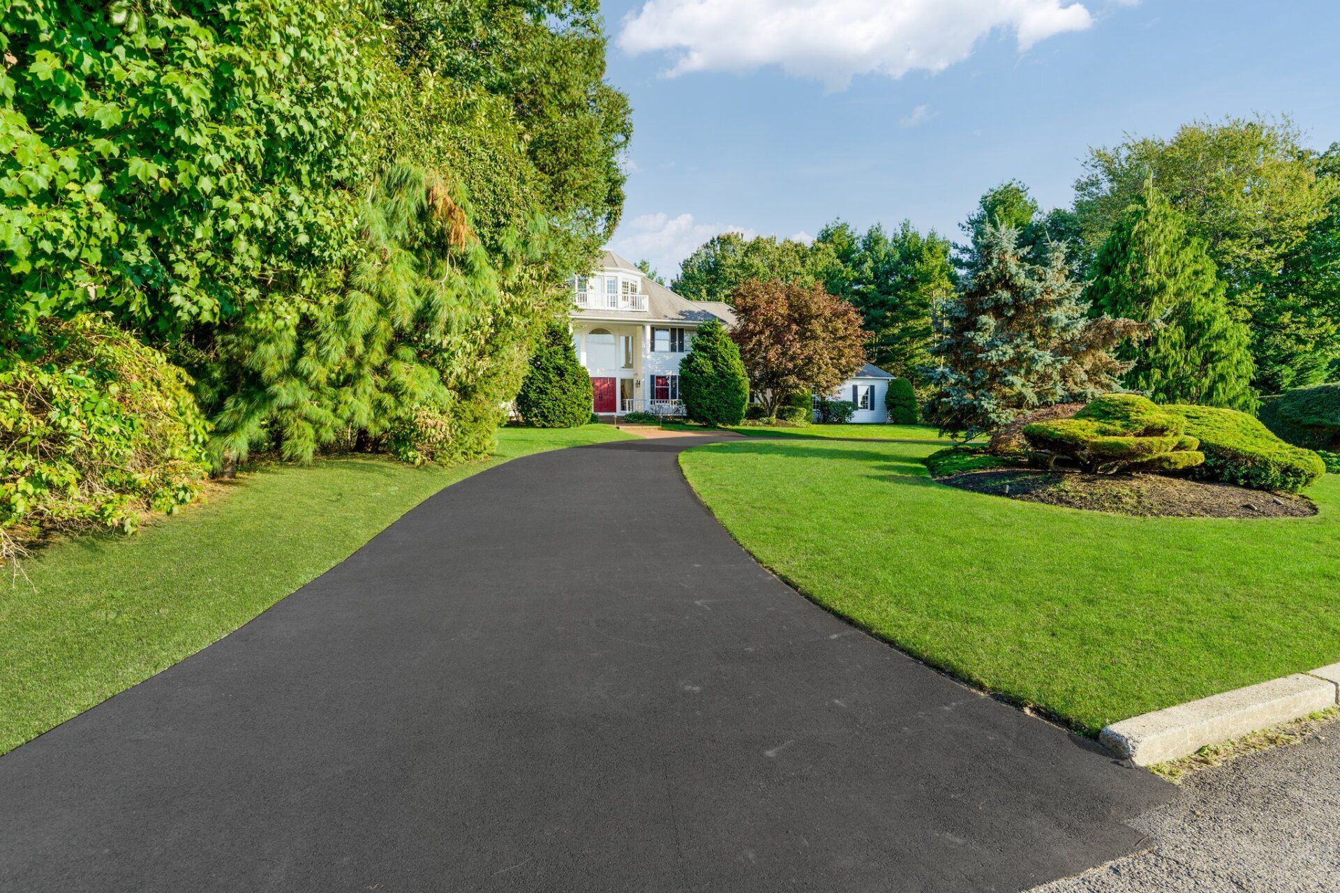 A driveway leading to a house surrounded by trees and grass