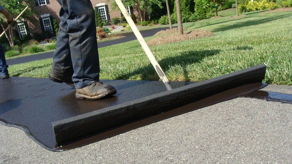 A person is spreading asphalt on a driveway with a rake