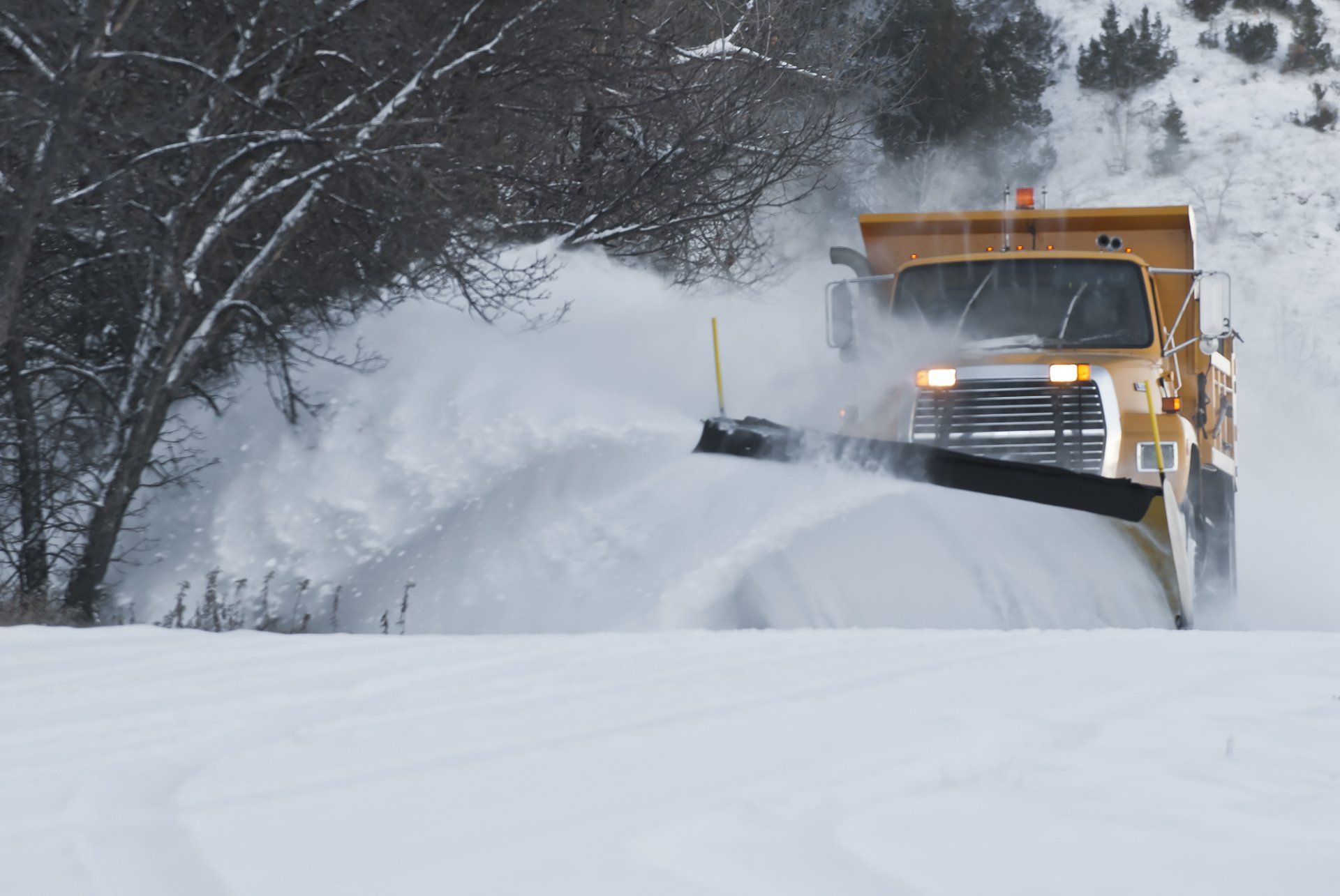 A snow plow is driving down a snowy road