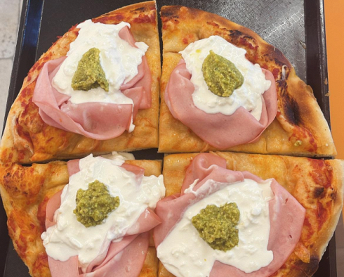 Una pizza con prosciutto e formaggio e pesto sopra