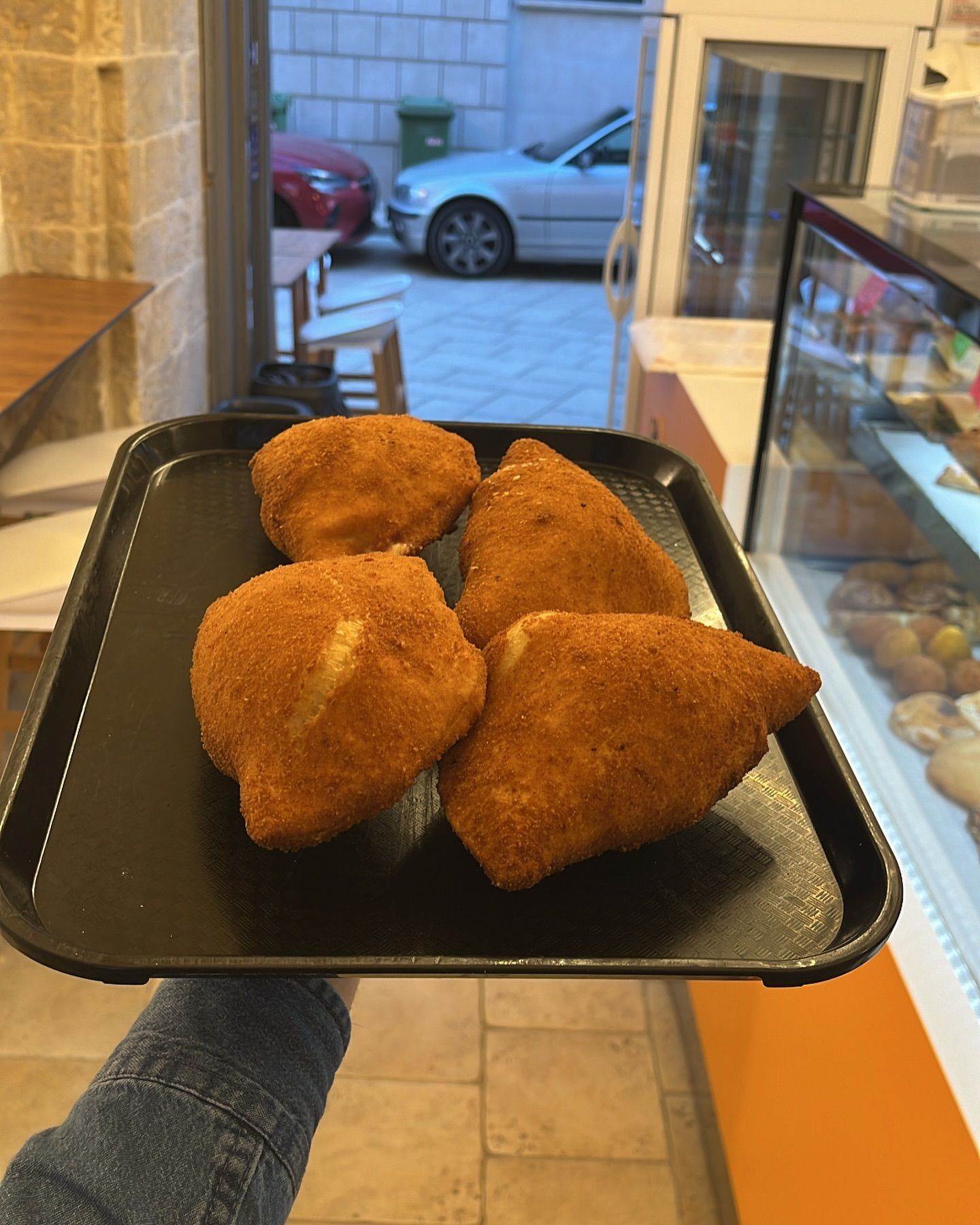 Una persona tiene in mano un vassoio nero con del cibo fritto sopra