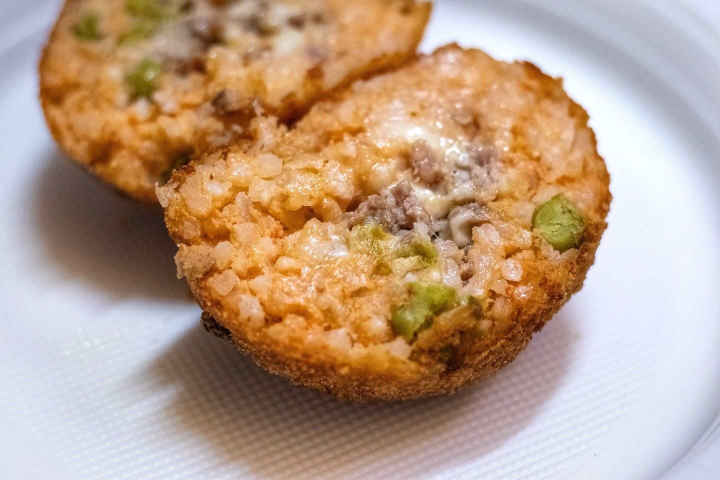 Due polpette di riso fritte con carne e piselli verdi su un piatto bianco.