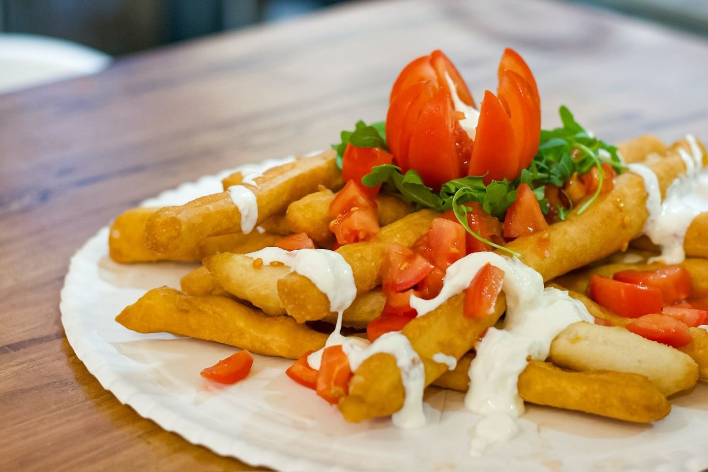 Un piatto di carta con patatine fritte e pomodori su un tavolo di legno.