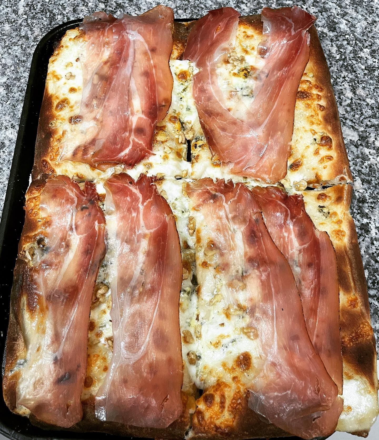 Una pizza con prosciutto e formaggio è appoggiata su un tavolo.